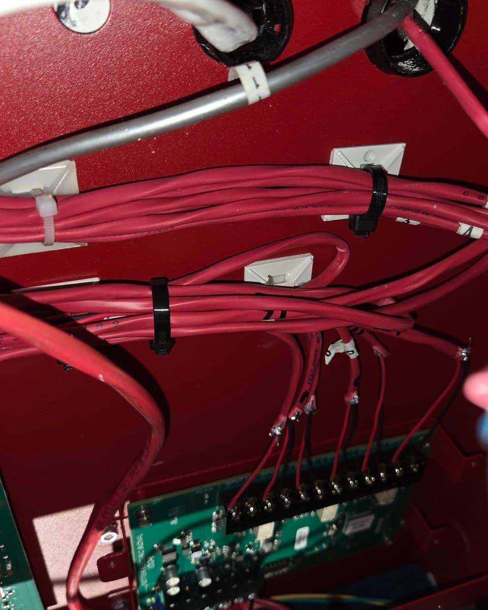 Red fire alarm cables bundled and terminated neatly on a circuit board inside a control panel