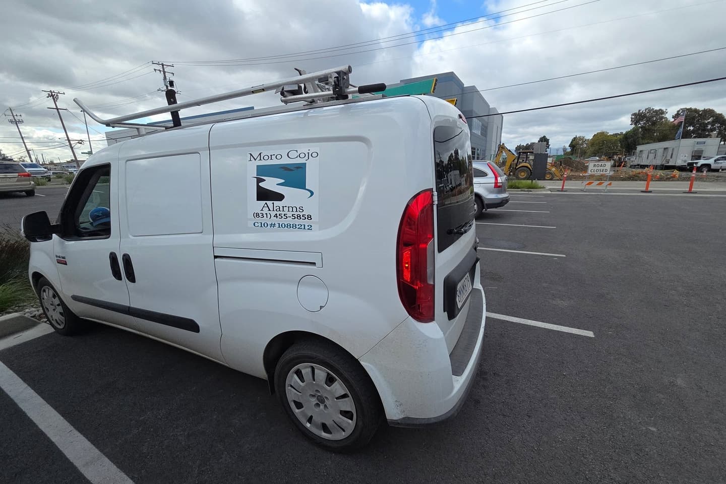 White Moro Cojo Alarms & Electric service van with the company logo and phone number on the door, parked at a job site